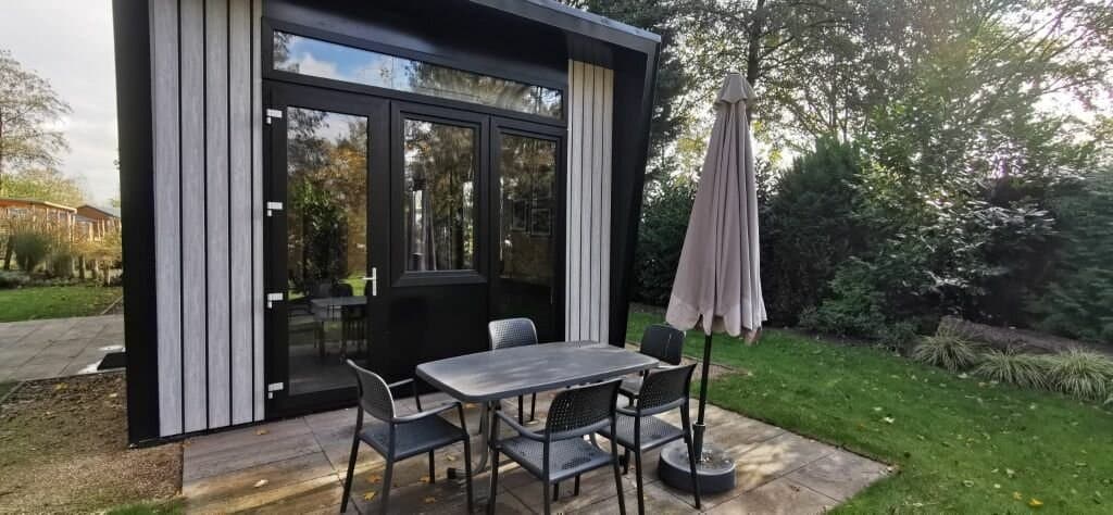 Terras met een tafel en stoelen voor een moderne woning, omgeven door groen en bomen in EuroParcs Zuiderzee