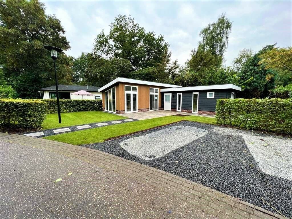 Moderne vakantiewoning met grote ramen, grasveld, bestrating en groene heggen aan de EuroParcs De Achterhoek