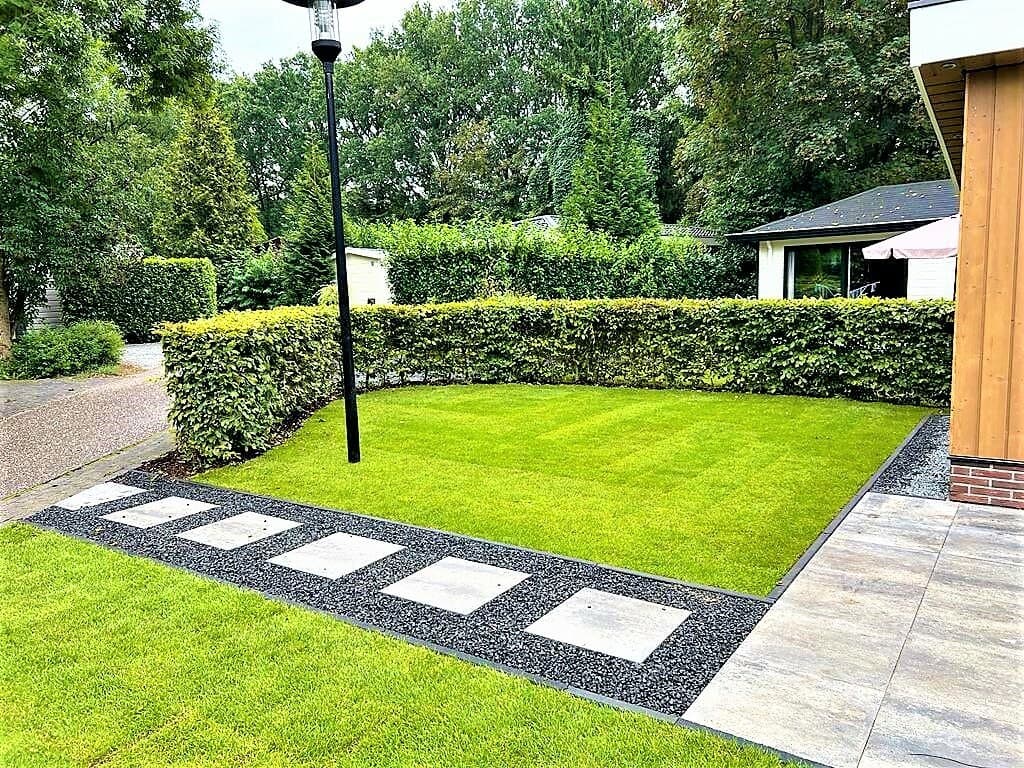 Groene tuin met geschoren haag, grasveld en betegeld pad bij EuroParcs De Achterhoek in Lochem.