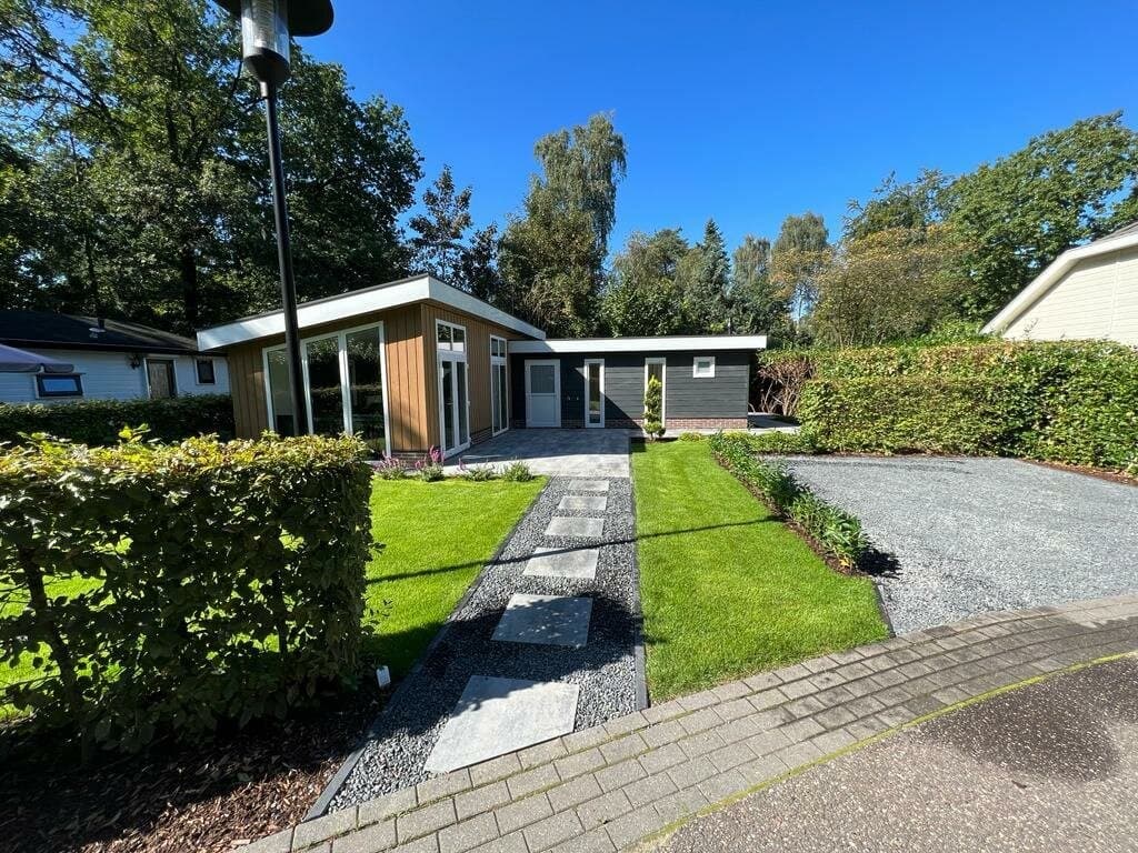 Moderne vakantiewoning omringd door groen, met een tuin en een grindpad naar de ingang.