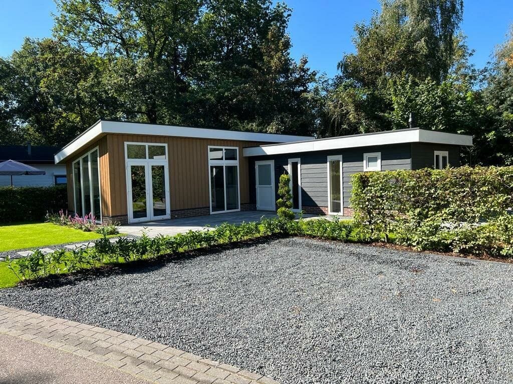 Moderne vakantiewoning met een houten gevel, grote ramen en aangelegde tuin met grind en groene struiken in EuroParcs De Acht