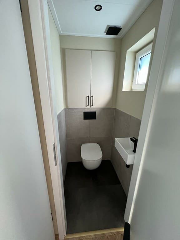 Kleine badkamer met toilet, wandkast en een raam voor natuurlijk licht.