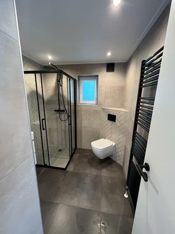 Moderne badkamer met inloopdouche, toilet en handdoekenradiator, afgewerkt met grijze tegels en lichte accenten