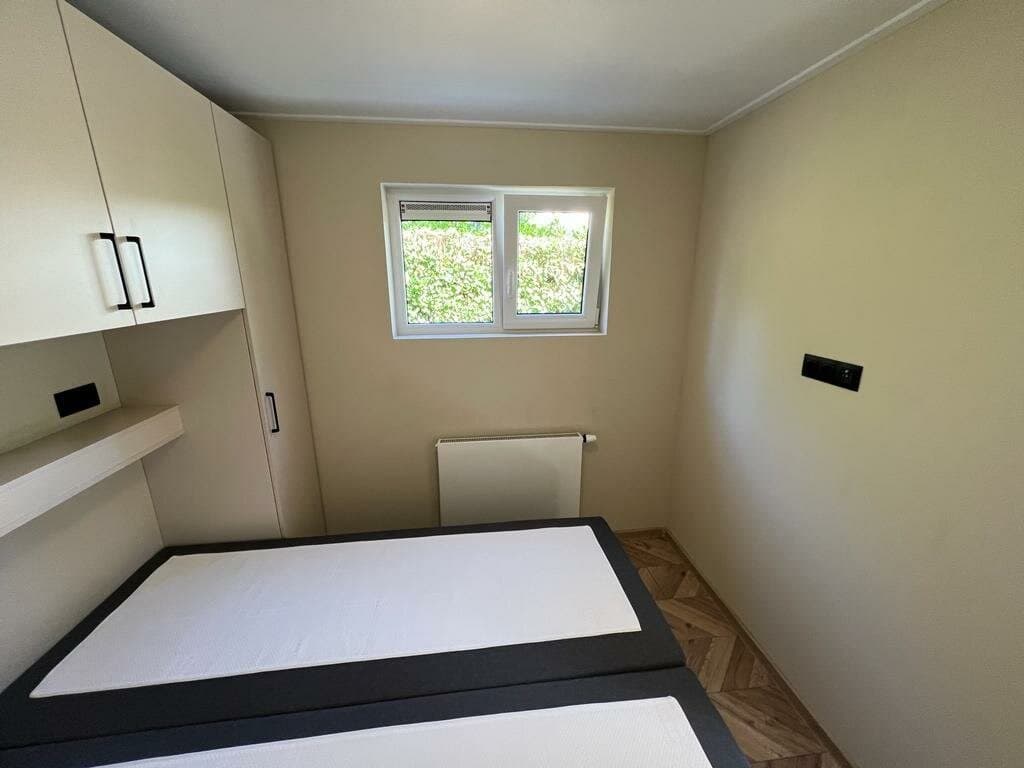 Slaapkamer met twee eenpersoonsbedden, een kast en een raam met uitzicht op de groene omgeving.