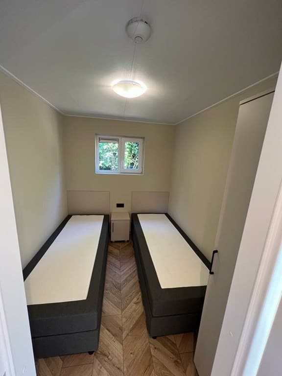 Slaapkamer met twee eenpersoonsbedden en een raam met uitzicht op groen, lichte muren en houtlook vloer.