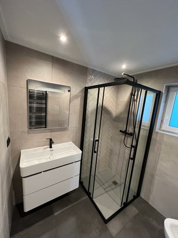 Moderne badkamer met inloopdouche, wastafel met kast en verwarmingselement aan de muur.