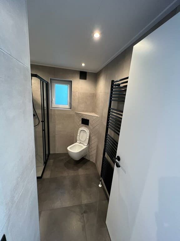 Moderne badkamer met douchecabine, toilet en handdoekradiator in neutrale kleuren.