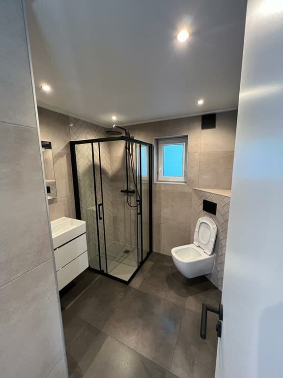 Moderne badkamer met inloopdouche, wastafel, toilet en lichte tegelafwerking.