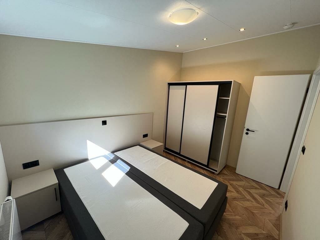 Slaapkamer met een dubbelbed, kledingkast en nachtkastje, lichte muren en houten vloer met een moderne uitstraling