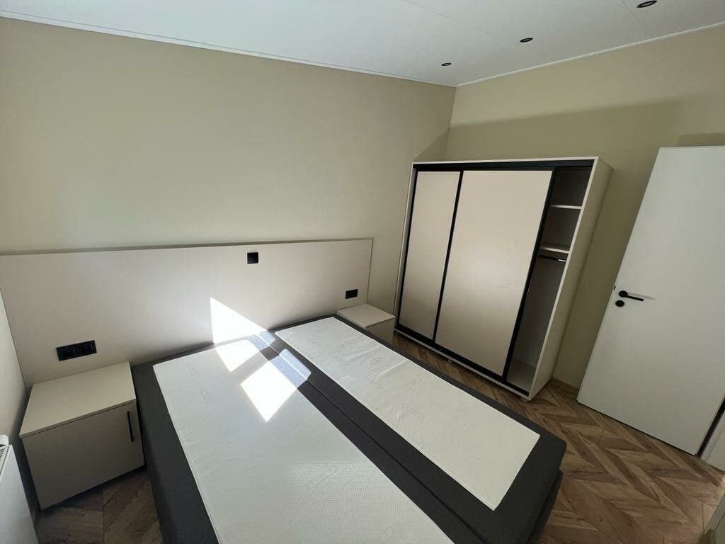 Slaapkamer met een tweepersoonsbed, kledingkast en nachtkastjes, lichte muren en een houten vloer.