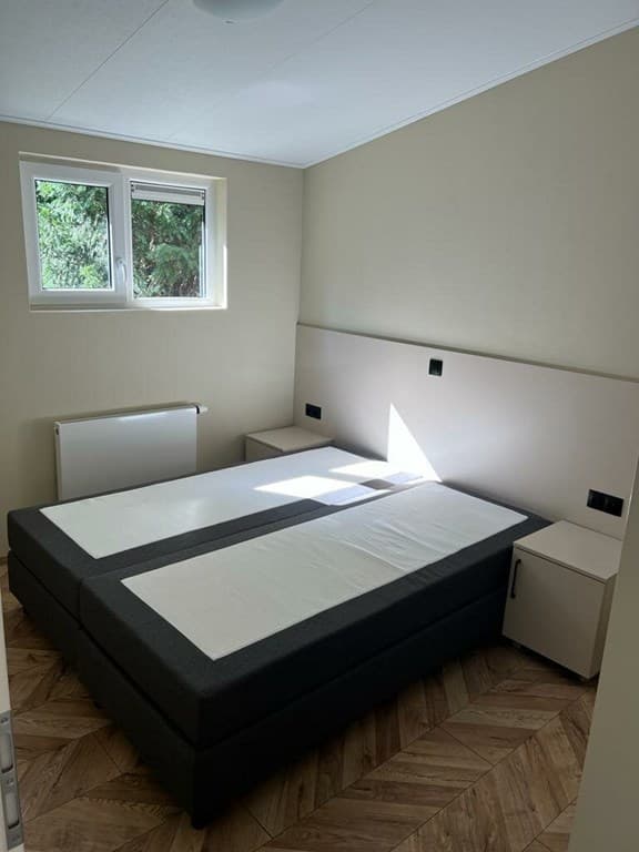 Slaapkamer met twee losse bedden, nachtkastjes en ramen die licht binnenlaten.