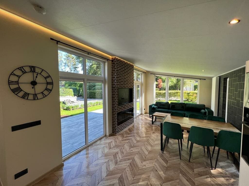 Lichtrijke woonruimte met een houten vloer, moderne meubels en grote ramen met uitzicht op de tuin.