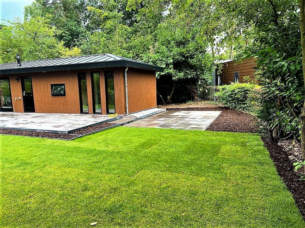 Moderne vakantiewoning met een groene tuin, bestrating en omringd door bomen en struiken.