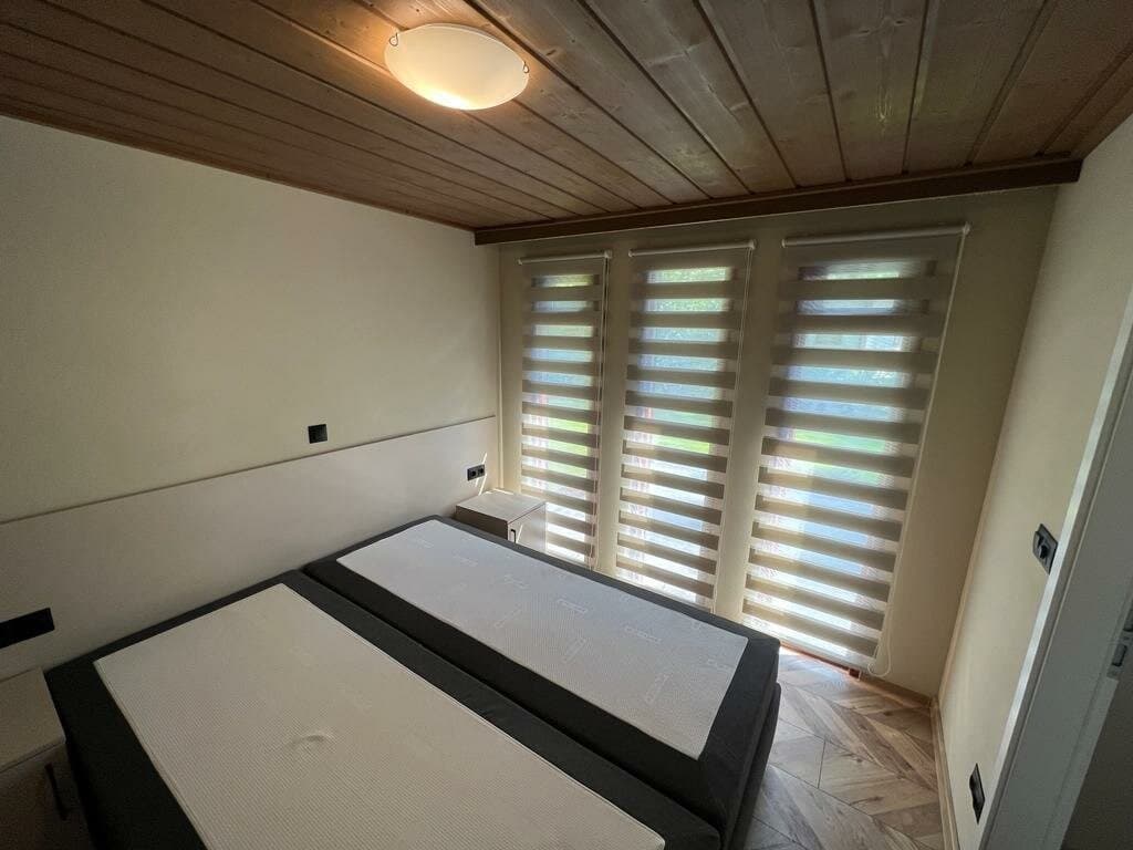 Slaapkamer met twee losse bedden, lamellen op het raam en een houten plafond.