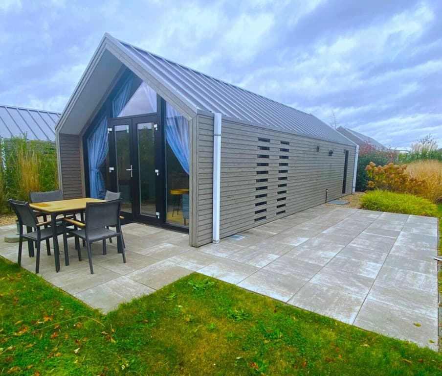 Moderne vakantiewoning met een stijlvolle houten gevel, terras en tuinmeubilair aan de voorzijde.