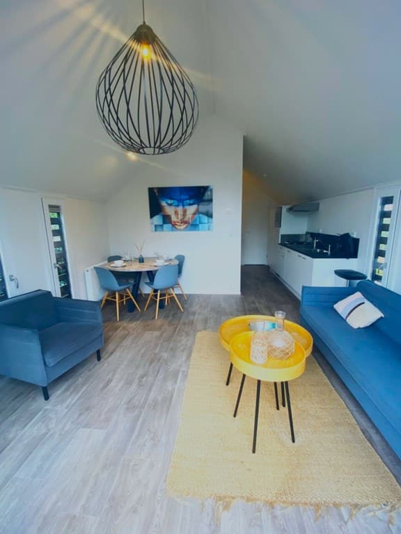 Moderne woonkamer met blauwe bank, eettafel met stoelen en een wanddecoratie boven een open keuken.