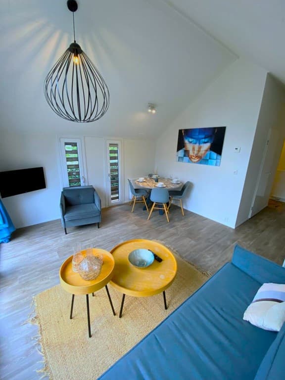 Moderne woonkamer met een blauwe bank, ronde tafel, kunst aan de wand en grote ramen met uitzicht op de buitenruimte
