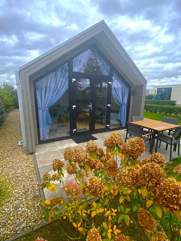 Vakantiehuis met groot glazen pui, terras met tafel en stoelen, en kleurrijke bloemen in de tuin.