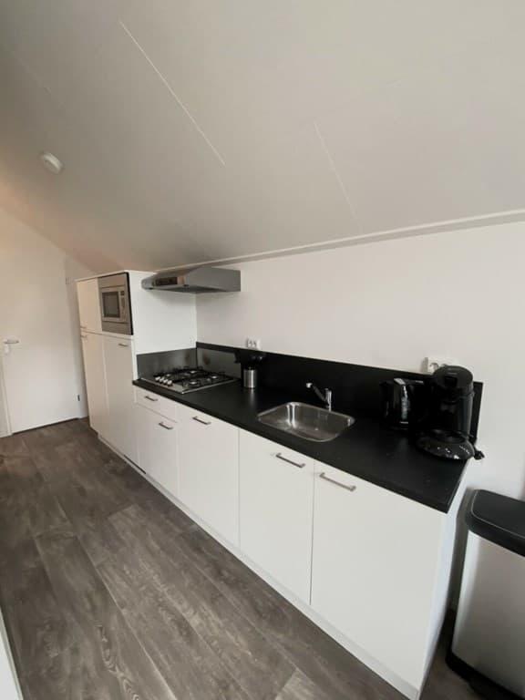 Kleine moderne keuken met donker aanrechtblad, kookplaat, oven en koelkast tegen een lichte wand.