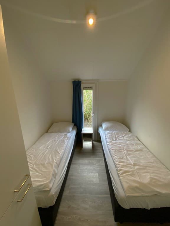 Slaapkamer met twee eenpersoonsbedden en een raam met uitzicht op groen.