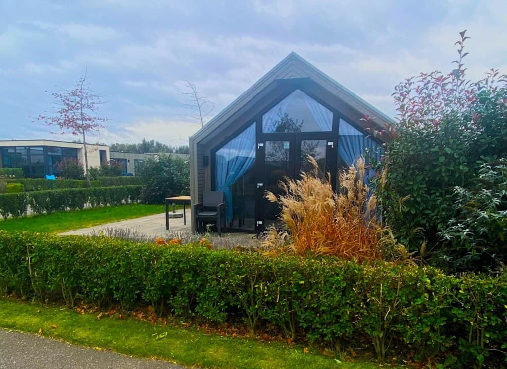 Vakantiehuis met een grote glaspartij, omringd door groene hagen en met een terras voor de deur