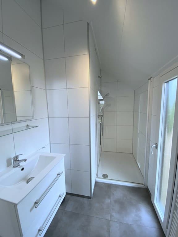 Moderne badkamer met inloopdouche, wastafel en grote wandspiegel in lichte kleuren en tegelvloer
