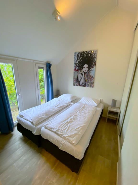 Slaapkamer met twee eenpersoonsbedden, groot schilderij aan de wand en ramen met groene tuin uitzicht.
