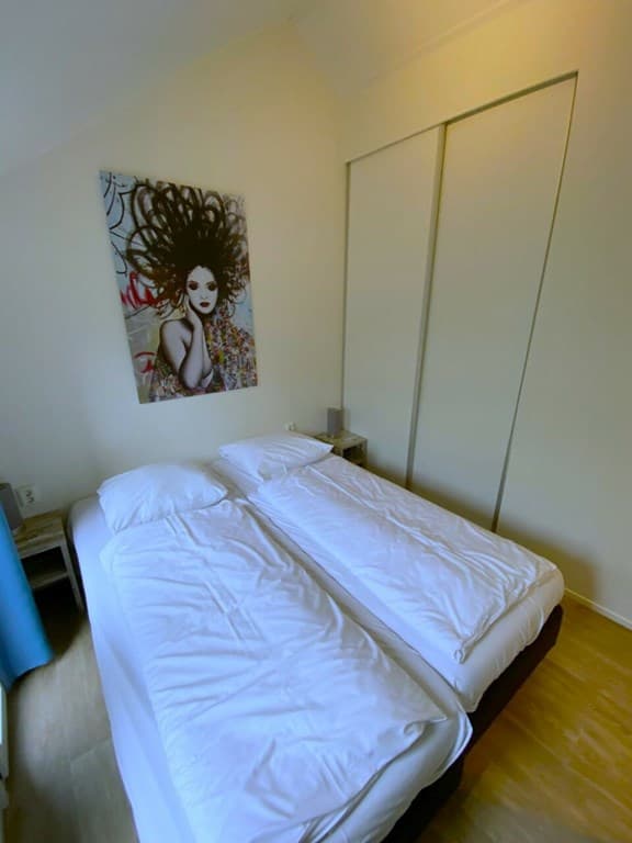 Slaapkamer met twee eenpersoonsbedden, lichte muren en een groot kunstwerk aan de muur.