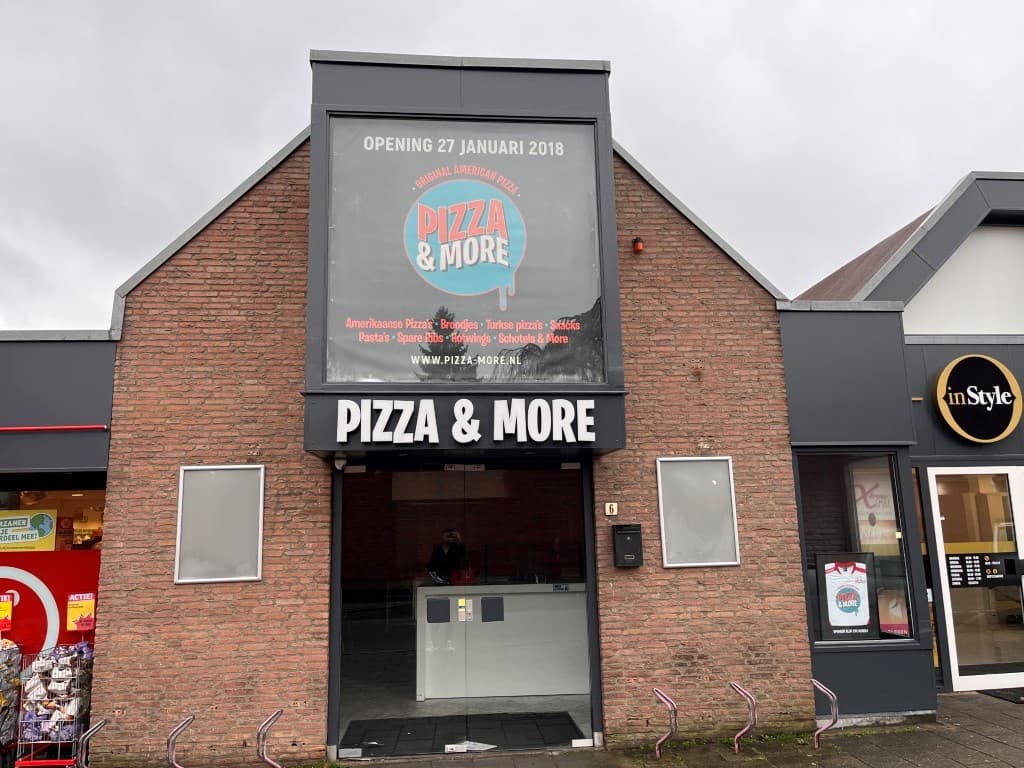 Gevel van een restaurant met een grote gevelsignering en een ruime ingangsdeur, omgeven door andere winkels