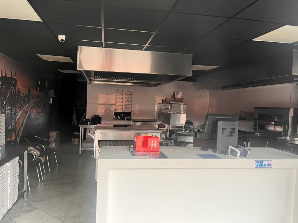 Ingerichte keuken met apparatuur, werkbladen en een kassasysteem in een lichte ruimte.