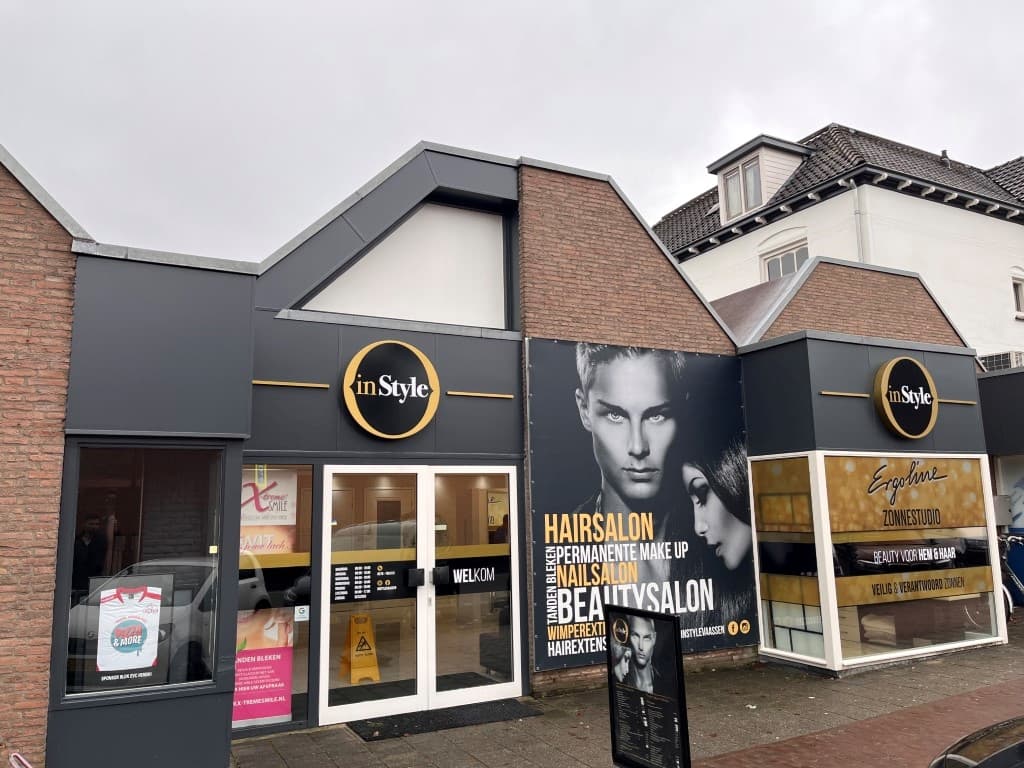 Voorkant van een modern gebouw met een kapsalon en beautysalon, grote ramen en een reclamebord met een model.