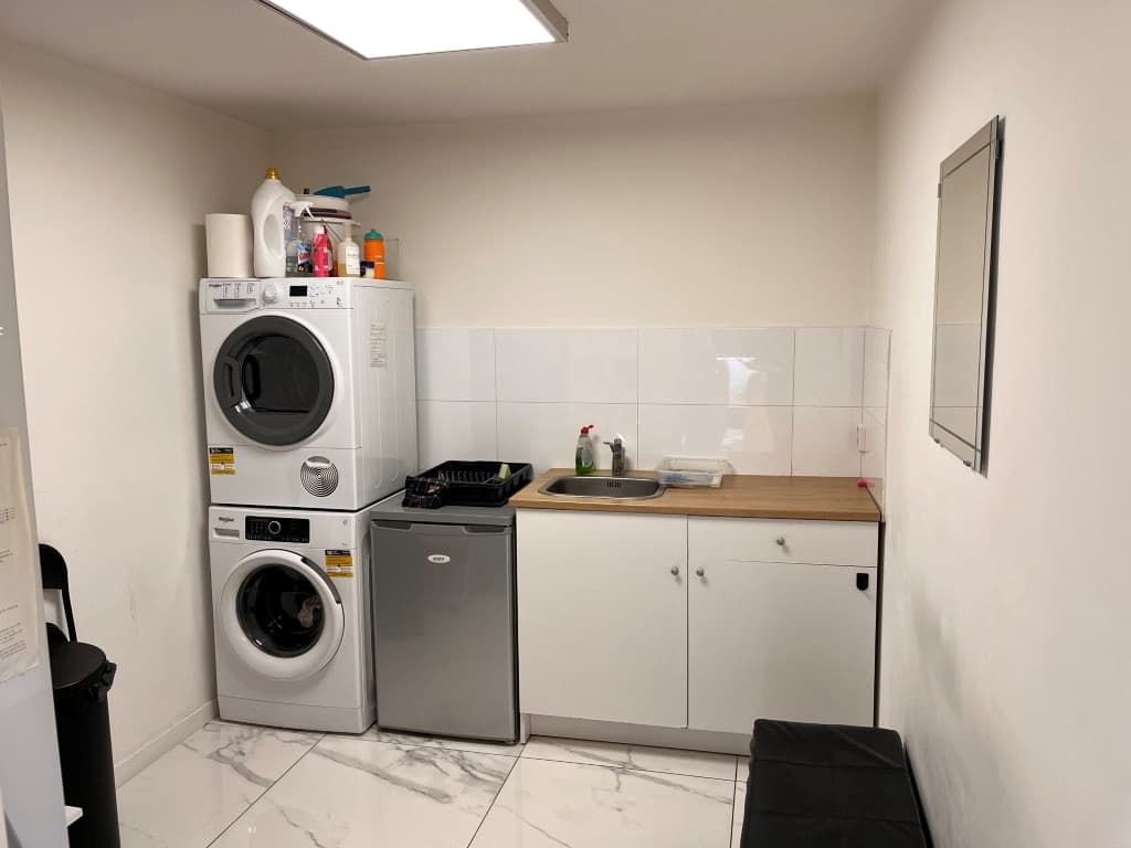 Keuken met wasmachine, droger, aanrecht, gootsteen en een koelkast in een appartement