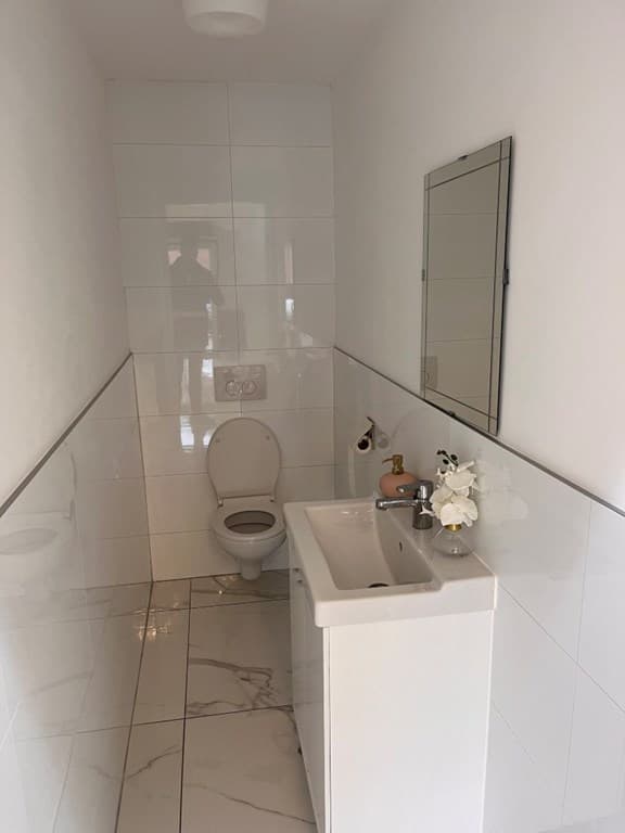 Lichte, betegelde badkamer met toilet, wastafel en spiegel aan de muur.