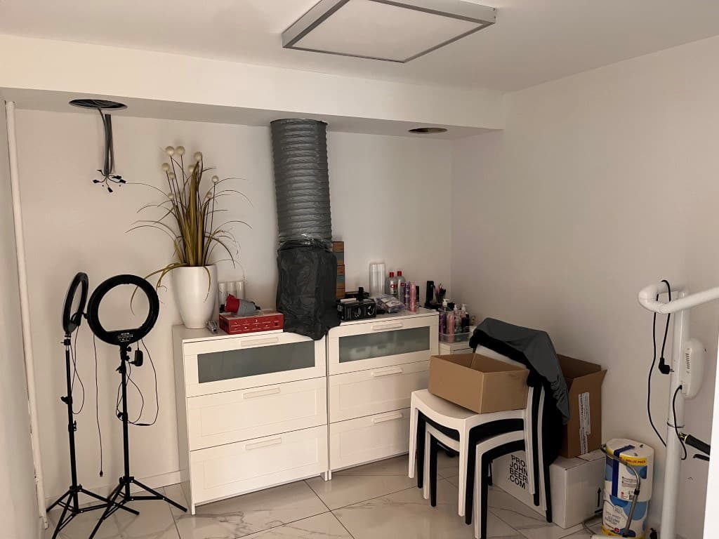 Een kamer met witte meubels, enkele stoelen, en dozen, met decoratieve elementen zoals een vaas en ligt apparatuur.