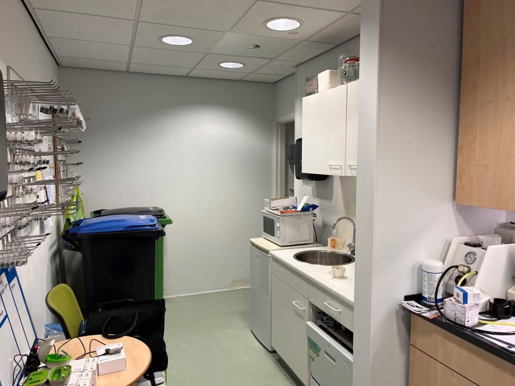 Keukenruimte met aanrecht, magnetron en afvalcontainers, naast een tafel met stoelen en wandrekken voor opslag.