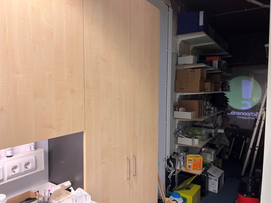 Ingerichte ruimte met houten kasten en planken vol spullen tegen de muur, helder verlicht met een projector op de achtergrond
