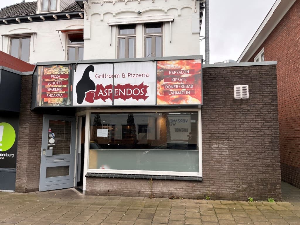 Voorgevel van het restaurant Aspendos met grote ramen en een geveldecoratie in een rustige straat.