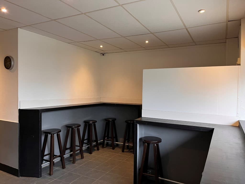 Interieur van een appartement met een barruimte en hoge houten stoelen aan een zwarte bar met lichte wanden.
