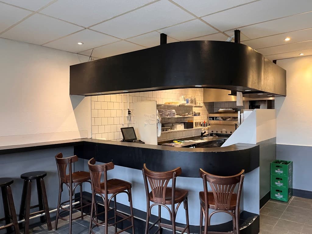 Open keuken met bar en houten barkrukken, metalen afwerking en overzichtelijke keukeninrichting zichtbaar.