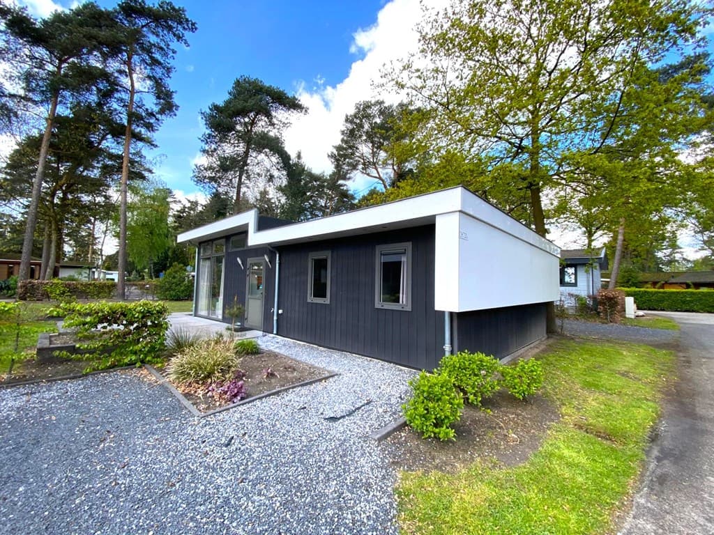 Moderne buitenaanzicht van een woning met grijze gevel en witte accenten, omringd door bomen en planten.