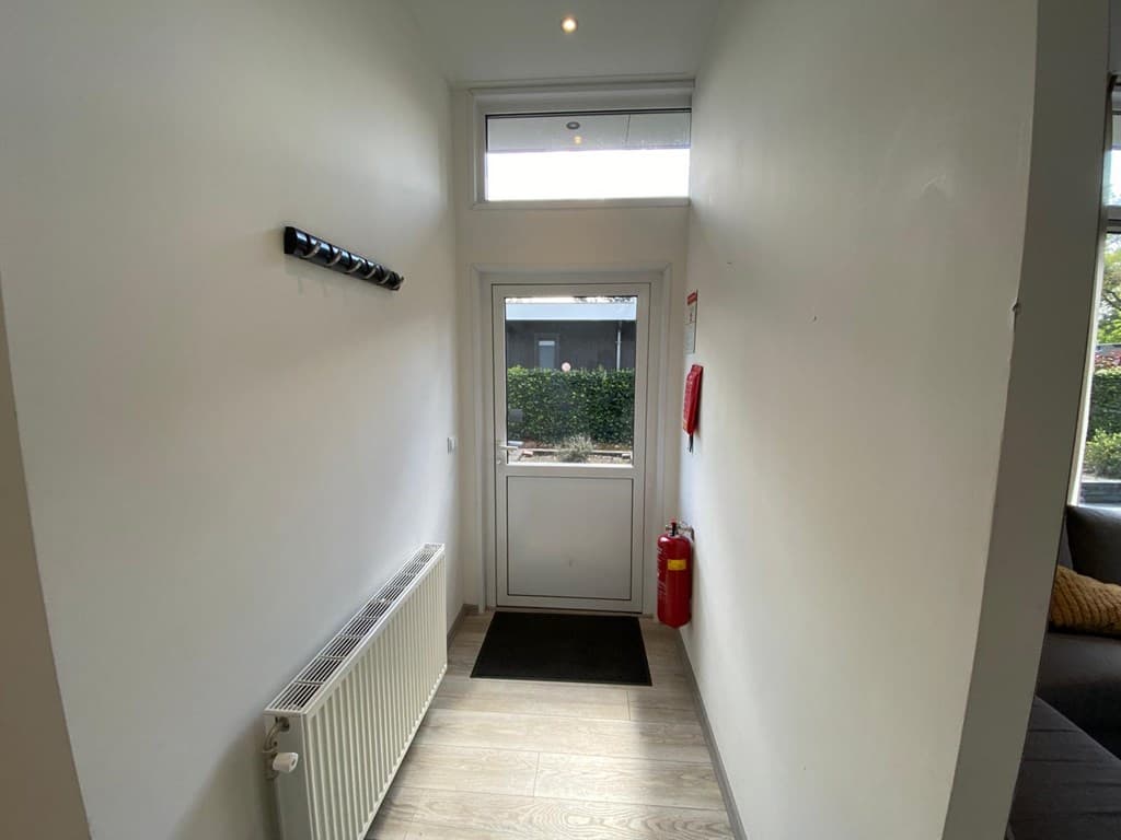 Hal met een deur naar buiten, een radiator, muurhaken en een brandblusser zichtbaar.