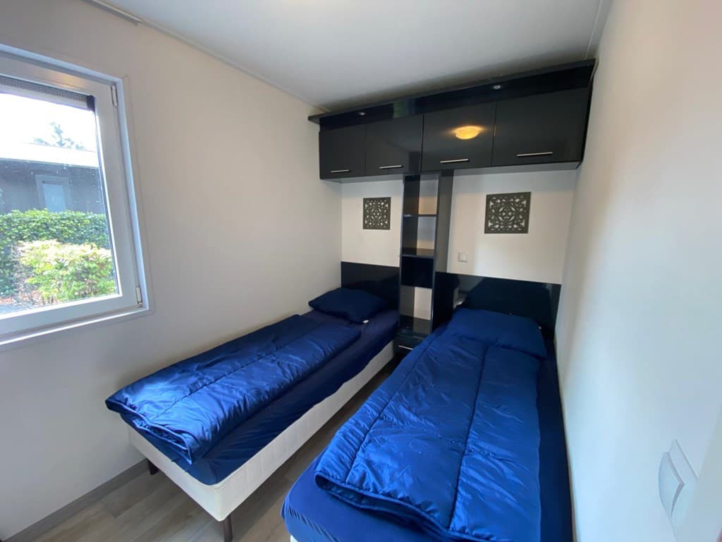 Slaapkamer met twee eenpersoonsbedden, donkerblauwe dekbedden en opbergruimte in kast boven de bedden.