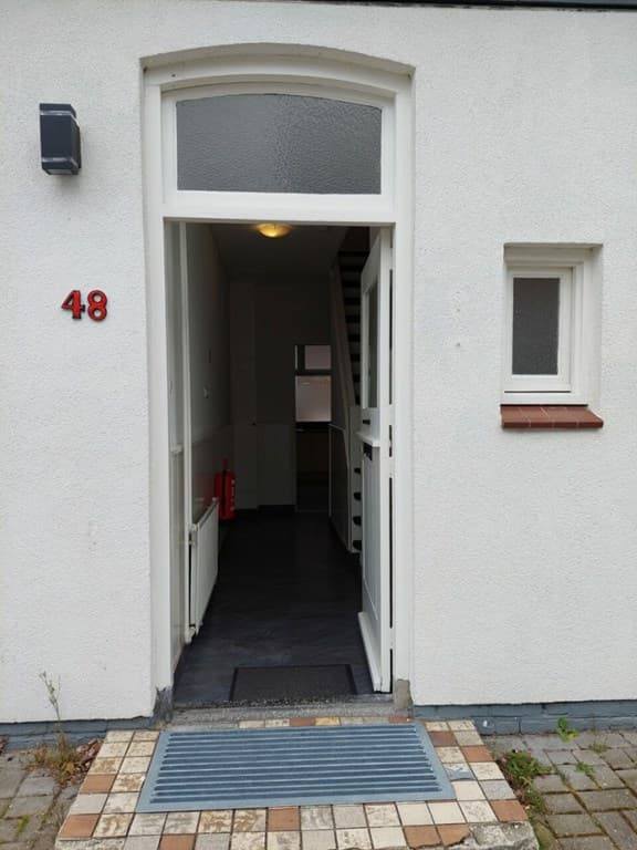 Entree van woning met een open deur, trap omhoog en tegelvloer zichtbaar, huisnummer 48 aan de gevel.