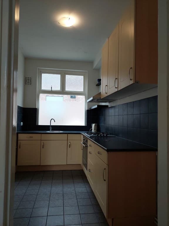 Keuken met lichtgekleurde kastjes, zwart aanrechtblad, gasfornuis en ramen voor natuurlijk licht.