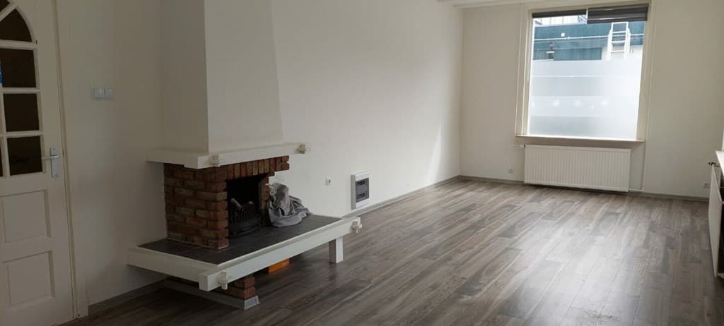 Woonkamer met laminaatvloer, een open haard en grote ramen voor natuurlijk licht