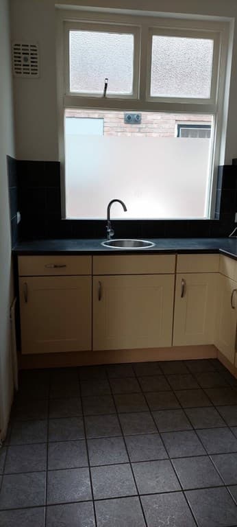 Keuken met wastafel, donkere wandtegels en lichte kasten, met een raam voor natuurlijk licht.