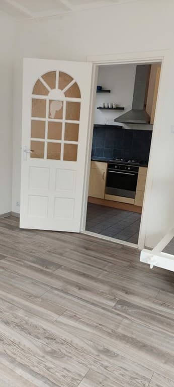 Interieur van een woning met een open deur naar de keuken en een houten vloer.