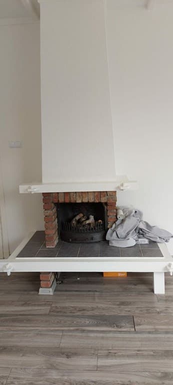Een schoorsteen met een stenen ombouw en een open haard, gelegen op een houten vloer met een grijze mat.