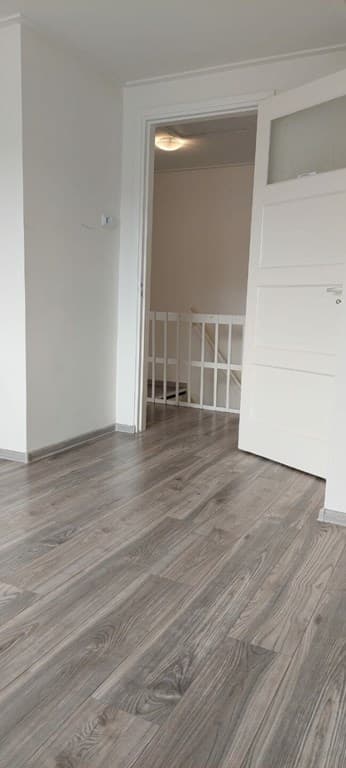 Binnenruimte met lichte wandafwerking en een houten vloer, open deur naar een trap en andere ruimte zichtbaar.