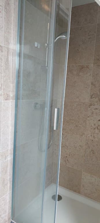 Douchecabine met glazen wand en moderne douchekop, betegelde wanden in neutrale tinten.